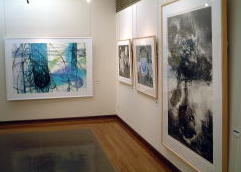 多摩美大版画OB展の会場風景。右は小泉健太郎さん「重すぎる乗客」、左は阿川理恵さん「青い柱」